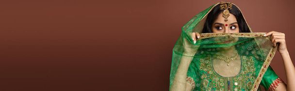 bonita mujer india con punto bindi en la frente cubriendo la cara con velo verde mirando hacia otro lado, pancarta - Foto, Imagen