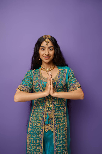 Ulusal kostümlü neşeli genç Hintli kadın dua ediyor ve kameraya bakıyor. - Fotoğraf, Görsel