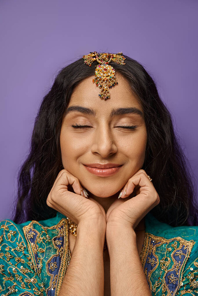 verticaal schot van aantrekkelijke indische vrouw in nationaal kostuum met gesloten ogen en handen onder kin - Foto, afbeelding