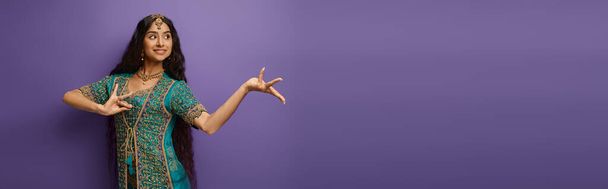 allegra donna indiana in abiti tradizionali gesticolando mentre ballava su sfondo viola, striscione - Foto, immagini
