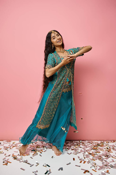 приваблива молода індійська жінка в традиційному костюмі посміхається на камеру, що стоїть на конфетті - Фото, зображення