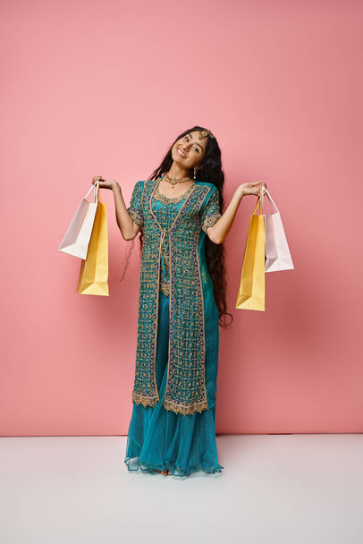 カメラで笑顔のショッピングバッグとポーズブルーサリの若いジョリーインディアン女性の垂直ショット - 写真・画像