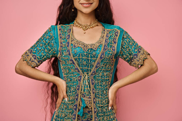 radosna młoda Hinduska kobieta w stroju narodowym pozuje z ramionami akimbo i uśmiecha się radośnie, przycięte - Zdjęcie, obraz