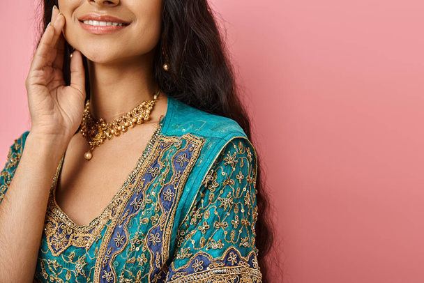 Ulusal kostümlü neşeli Hintli kadın pembe arka planda eli yüzü yere yakın gülümsüyor. - Fotoğraf, Görsel