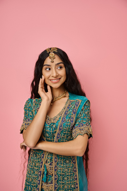 вертикальный снимок привлекательной веселой индианки, позирующей с рукой рядом с лицом и смотрящей в сторону - Фото, изображение