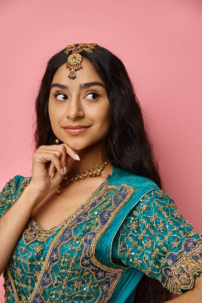 vertical shot of pretty indian woman in national costume posing on pink backdrop with hand on chin - 写真・画像