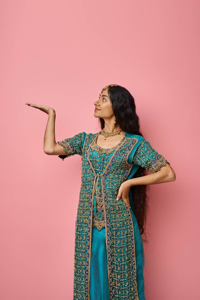 美しい若いインドの女性の垂直ショットは,オープンパームを探してポーズする民族衣装 - 写真・画像