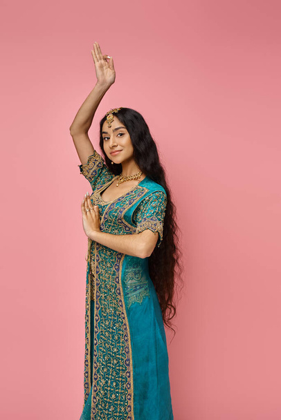 krásná indická žena v modrém sárí s doplňky gestikulující na růžovém pozadí při pohledu do kamery - Fotografie, Obrázek