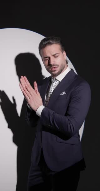 side view video of handsome bearded man looking to side, rubbing palms and fixing suit, touching chin and being thoughtful in front of round spotlight on grey background - Footage, Video