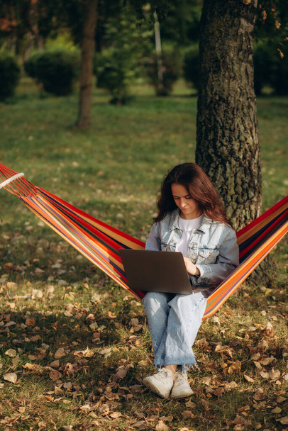 Jovem mulher bonita deitada em uma rede com laptop em um jardim. fundo verde. Árvores teletrabalho. trabalho remoto. Foto de alta qualidade - Foto, Imagem