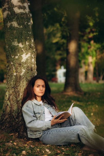 Młoda kobieta czyta książkę pod drzewem podczas pikniku w wieczornym słońcu. Wysokiej jakości zdjęcie - Zdjęcie, obraz