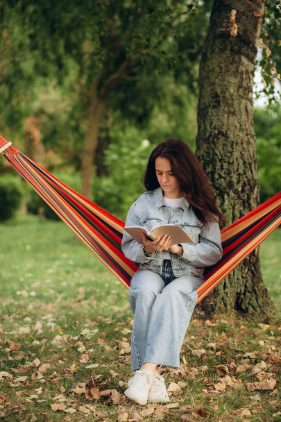 Молода жінка читає книгу в зручному гамаку в зеленому саду. Високоякісна фотографія - Фото, зображення