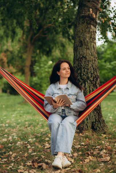 緑の庭で快適なハンモックで本を読んでいる若い女性. 高品質の写真 - 写真・画像