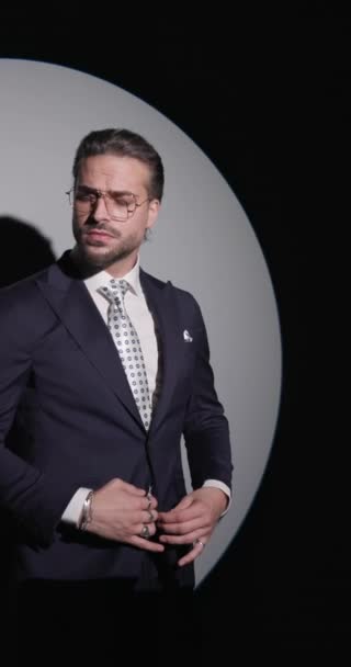 Hochklassiger Geschäftsmann mit Brille, marineblauem Anzug, wegschauen, sich in Seiten- und Rückansicht bewegen und vor grauem Hintergrund posieren - Filmmaterial, Video
