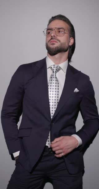 cool fashion zakenman met bril, hand in hand zak, op zoek naar kant, aanpassen pak, aanraken kin en denken op grijze achtergrond - Video