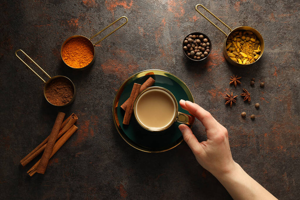 Masala té, especias y mano sobre fondo gris oscuro, vista superior - Foto, Imagen