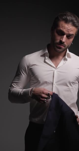 ελκυστική υψηλής κατηγορίας επιχειρηματίας κρατώντας σακάκι πάνω από τον ώμο και να είναι σίγουροι μπροστά από γκρι φόντο - Πλάνα, βίντεο
