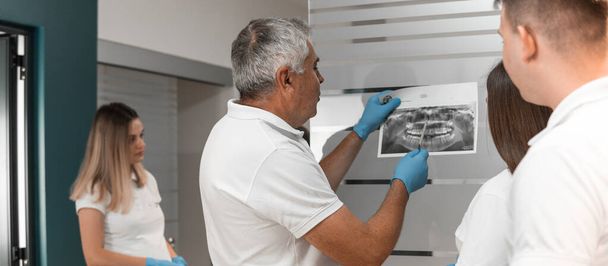 Zespół dentystów bada prześwietlenia rentgenowskie, rezonans zębów jamy ustnej, omawia metody leczenia i wykonalność implantów w ośrodku stomatologicznym. Wysokiej jakości zdjęcie - Zdjęcie, obraz
