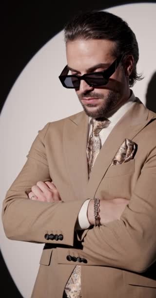 sexy hochklassiger junger Mann mit Sonnenbrille, die Arme verschränkt, nach vorne schauend und selbstbewusst auf grauem Hintergrund - Filmmaterial, Video