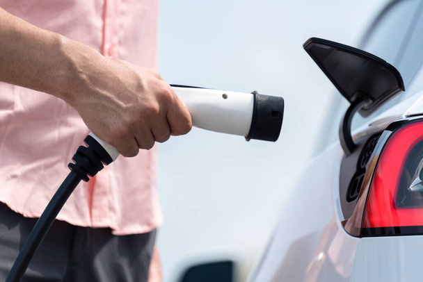 Stecken Sie das Ladegerät per Hand in das Elektrofahrzeug, um die Batterie des Elektroautos an einer Außenladestation aufzuladen. Frisches Tageslicht mit alternativem, sauberem und nachhaltigem Energiekonzept. Unvergänglich - Foto, Bild