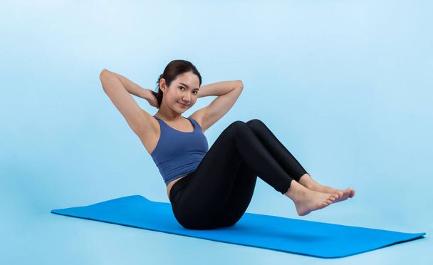 Asian woman in sportswear doing crunch on exercising mat as workout training routine. Attractive girl in pursuit of healthy lifestyle and fit body physique. Studio shot isolated background. Vigorous - Photo, Image
