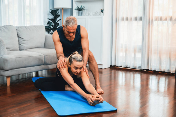 Ευτυχισμένο ενεργό ζευγάρι ηλικιωμένων στο αθλητικό ντύσιμο είναι υποστηρικτική και να βοηθήσει στη στάση γιόγκα μαζί στο σπίτι. Υγιής ηλικιωμένος άνδρας και γυναίκα τρόπο ζωής με άσκηση γιόγκα. Μύγα - Φωτογραφία, εικόνα