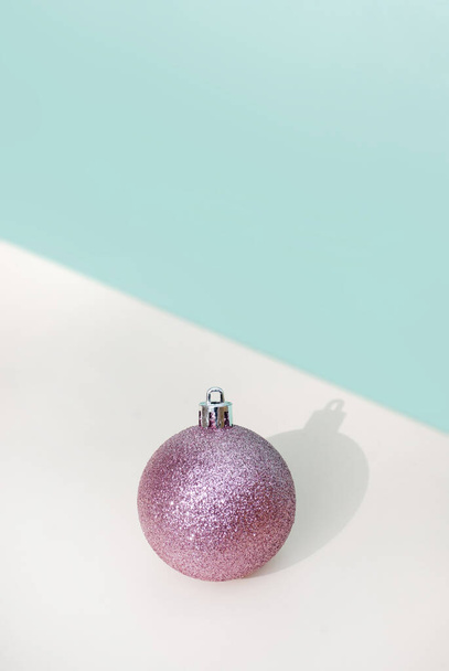 Rosa glitter palla decorazione di Natale su uno sfondo blu tavolo beige con ombra. Minimale concetto di vacanze invernali. Ricevuto. Spazio per testo - Foto, immagini