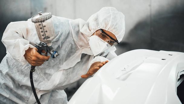 Automotive service worker in full protective gear expertly apply color paint in to cars bodywork with spray gun or respirator painting in chamber workshop. Car paint service for scratch refinish.Oxus - Photo, Image