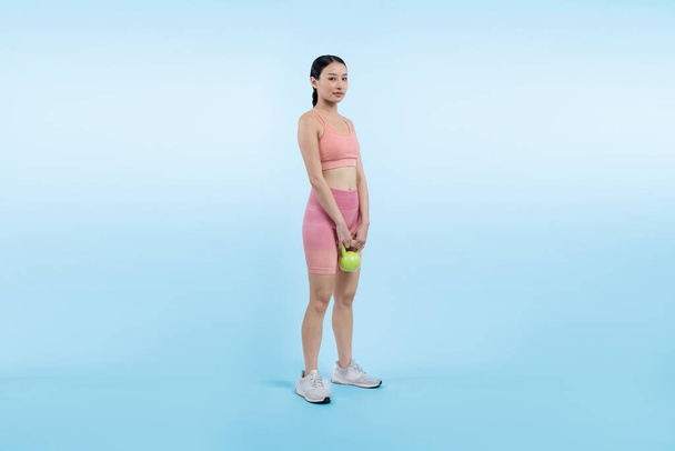 Energische, energische Frau, die auf isoliertem Hintergrund eine Kettlebell-Gewichtheben-Übung macht. Junge athletische asiatische Frau Kraft- und Ausdauertraining als Körpertraining-Routine. - Foto, Bild
