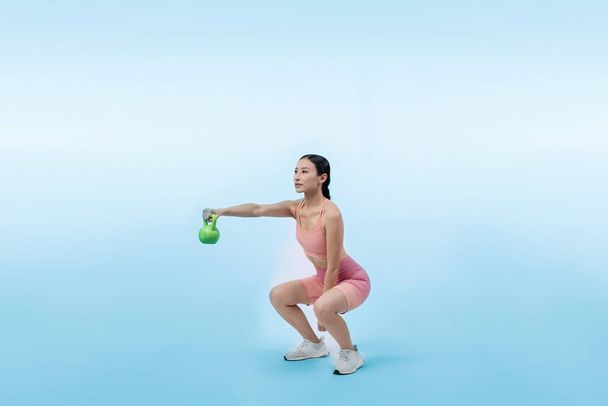 Energische, energische Frau, die auf isoliertem Hintergrund eine Kettlebell-Gewichtheben-Übung macht. Junge athletische asiatische Frau Kraft- und Ausdauertraining als Körpertraining-Routine. - Foto, Bild
