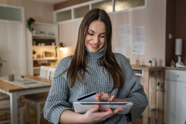 Eine erwachsene kaukasische Frau sitzt zu Hause glücklich lächeln halten digitale Tablette halten Bankkreditkarte Online-Shopping-Konzept echte Menschen kopieren Raum E-Commerce - Foto, Bild