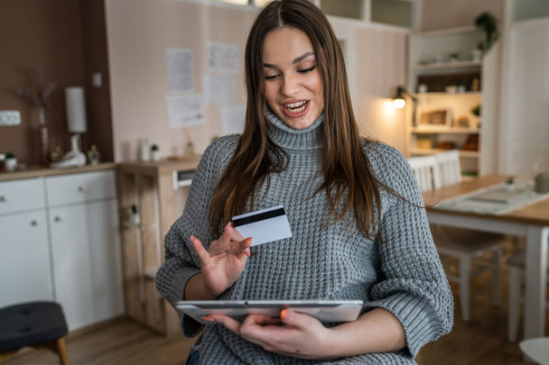 Jedna kobieta dorosła kaukaska kobieta siedzieć w domu szczęśliwy uśmiech trzymać cyfrowy tablet trzymać bank karta kredytowa koncepcja zakupów online prawdziwi ludzie kopiować przestrzeń e-commerce - Zdjęcie, obraz