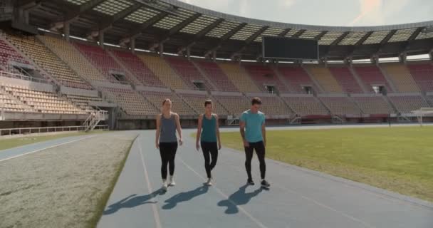 Tre persone che camminano verso la pista dello stadio - Filmati, video