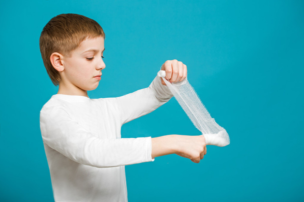 Boy in white clothes taping up bandage on his thumb - 写真・画像