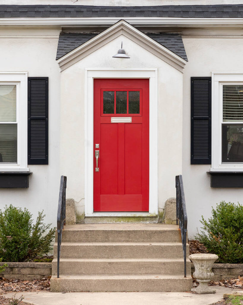 Un détail de porte d'entrée rouge sur une maison blanche avec marches en béton et balustrades en fer menant à la porte. - Photo, image