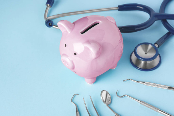 Банк розовых свиней с инструментами стоматолога на синем фоне, копировальное пространство - Фото, изображение