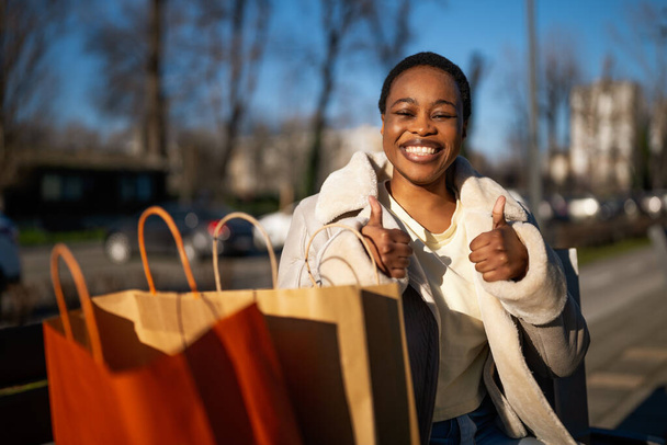 Ulkomuotokuva onnellisesta mustasta naisesta. Hän istuu penkillä kadulla ostosten jälkeen.. - Valokuva, kuva