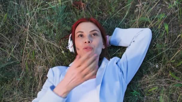 niezależny pracownik, młoda kobieta rozmawiająca za pomocą słuchawki z klientem leżącym na polanie w parku, widok z góry - Materiał filmowy, wideo