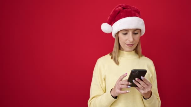 Junge blonde Frau lächelt selbstbewusst und trägt Weihnachtsmütze über rotem Hintergrund - Filmmaterial, Video