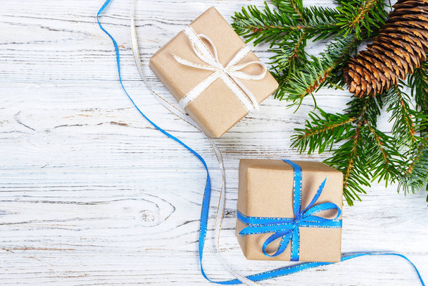 Рождественская подарочная коробка на белом фоне деревянного стола, еловая ветвь, сосновые шишки, рамка, вид сверху, место для текста
. - Фото, изображение