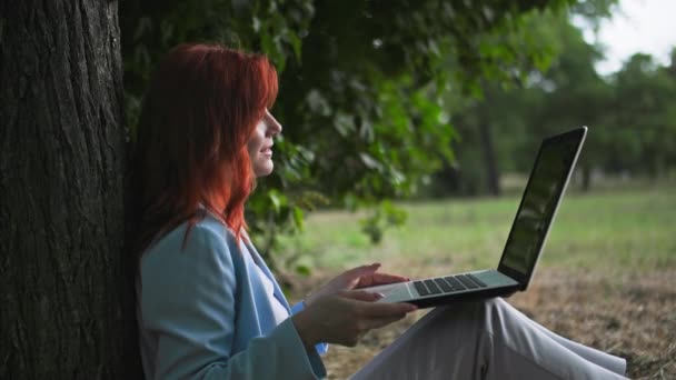 szabadtéri iroda, gyönyörű nő dolgozik távolról beszél videohívás Clint ül közel fa a parkban - Felvétel, videó