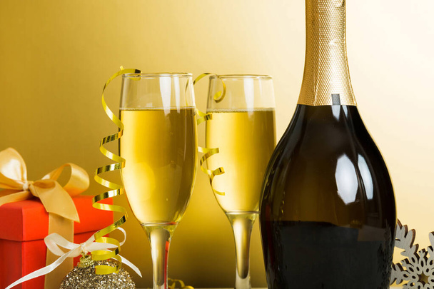 Бутылка шампанского с конфетти, бокалы и рождественский декор на цветном фоне праздника. Новогодние украшения. - Фото, изображение
