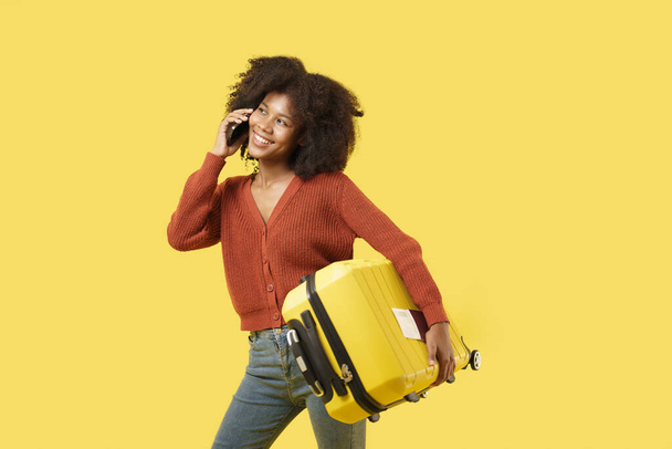 Afroamerikanische junge Frau in lässigem Lebensstil mit gelbem Gepäck sieht beim Telefonieren aufregend aus. - Foto, Bild