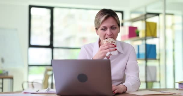 Woman manager eating shawarma at table in front of laptop 4k movie slow motion. Meal break at work concept - Footage, Video