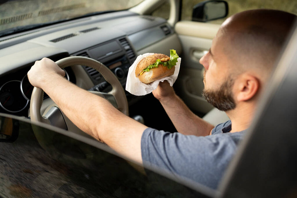 Mężczyzna je śniadanie i jeździ samochodem. Kolacja w samochodzie. Przednie siedzenie. Koncepcja jedzenia. Przestrzeń kopiowania - Zdjęcie, obraz