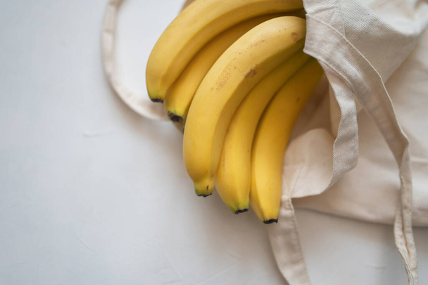 Sweet Ripe yellow bananas in shopping bag on table white background. Healthy tropical food. - Photo, Image