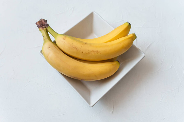 Два спелых жёлтых банана на белой тарелке. белый фон. Вид сверху. - Фото, изображение