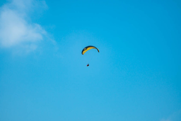 Ένα άθλημα που αντλεί αδρεναλίνη, παραπαίοντας στον καταγάλανο ουρανό. Αλεξίπτωτο που πετάει με το αλεξίπτωτο του πάνω από τον ουρανό με φόντο τον γαλάζιο ουρανό και τα άσπρα σύννεφα σε μια ηλιόλουστη μέρα. - Φωτογραφία, εικόνα