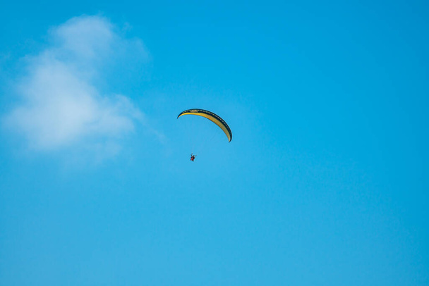 Un deporte extremo que bombea adrenalina, parapente contra el cielo azul claro. Parapente volando con su paracaídas sobre el cielo con un fondo de cielo azul y nubes blancas en un día soleado. - Foto, imagen