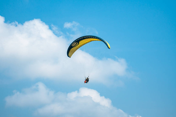 An adrenaline-pumping extreme sport, paragliding against the clear blue sky. Paraglider flying with his parachute above the sky with a background of blue sky and white clouds in a sunny day. - Photo, Image
